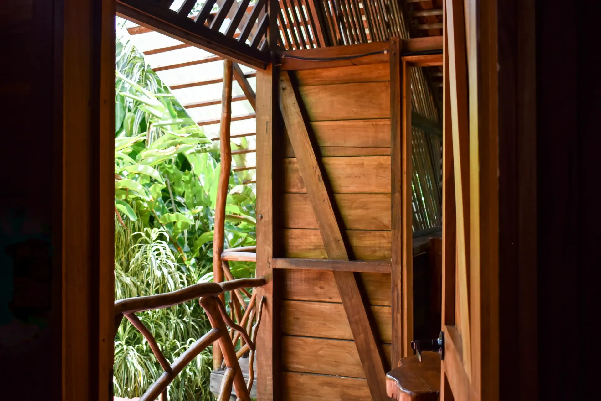 Wooden cabin interior with a balcony overlooking lush green foliage.