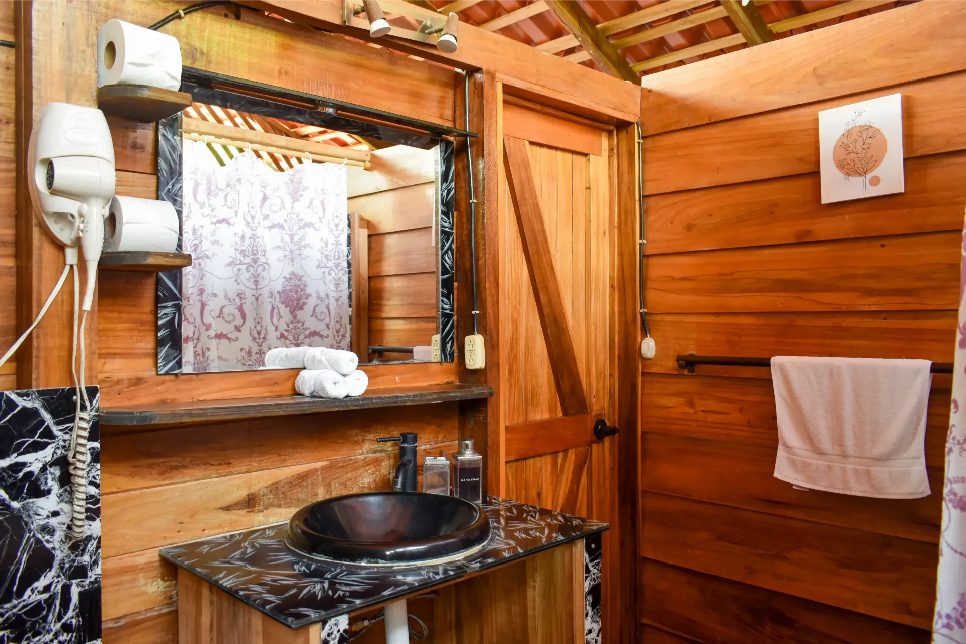 Wooden bathroom with a dark sink, mirror, and towel rack.