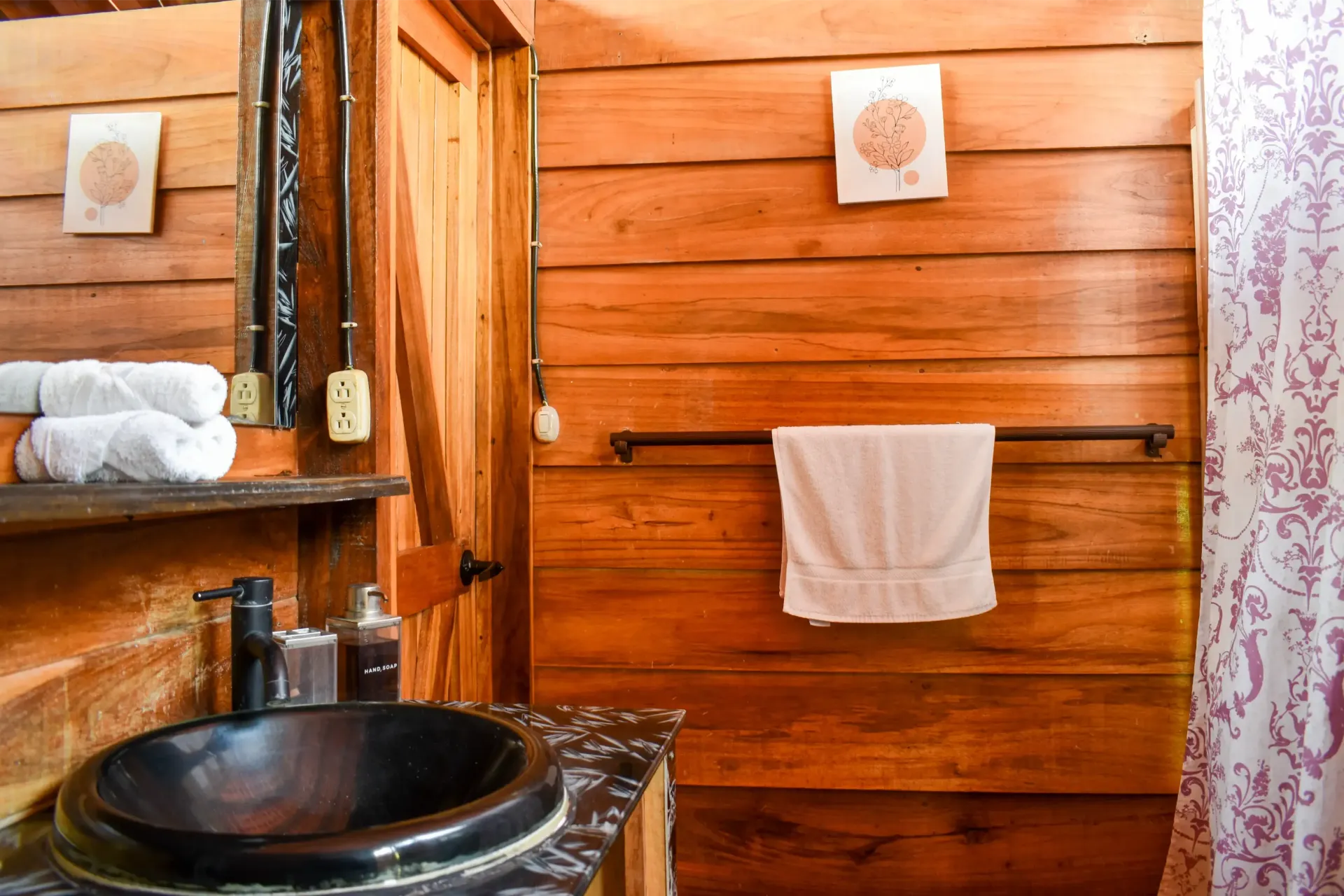 Wooden bathroom with black sink, white towels, and decorative wall art.