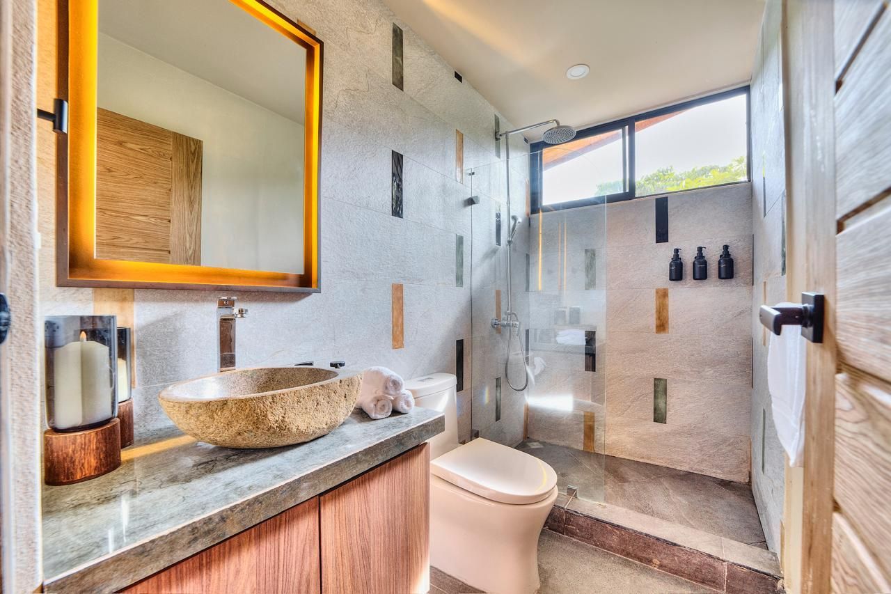 Bathroom with stone sink, shower, and toilet, featuring textured walls and wooden accents.