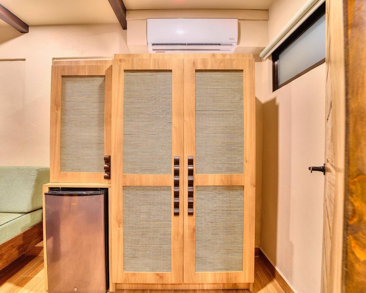 Wooden wardrobe, refrigerator, and air conditioner in a room with a window and a door.