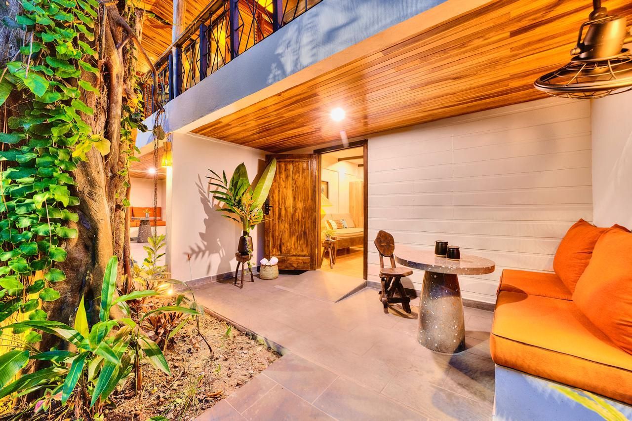 Outdoor seating area with orange cushions, wooden ceiling, and lush greenery.