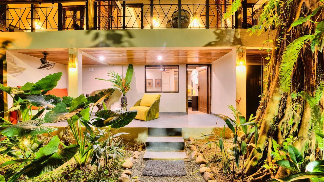 Two-story building with a porch, plants, and an armchair. Night lighting.
