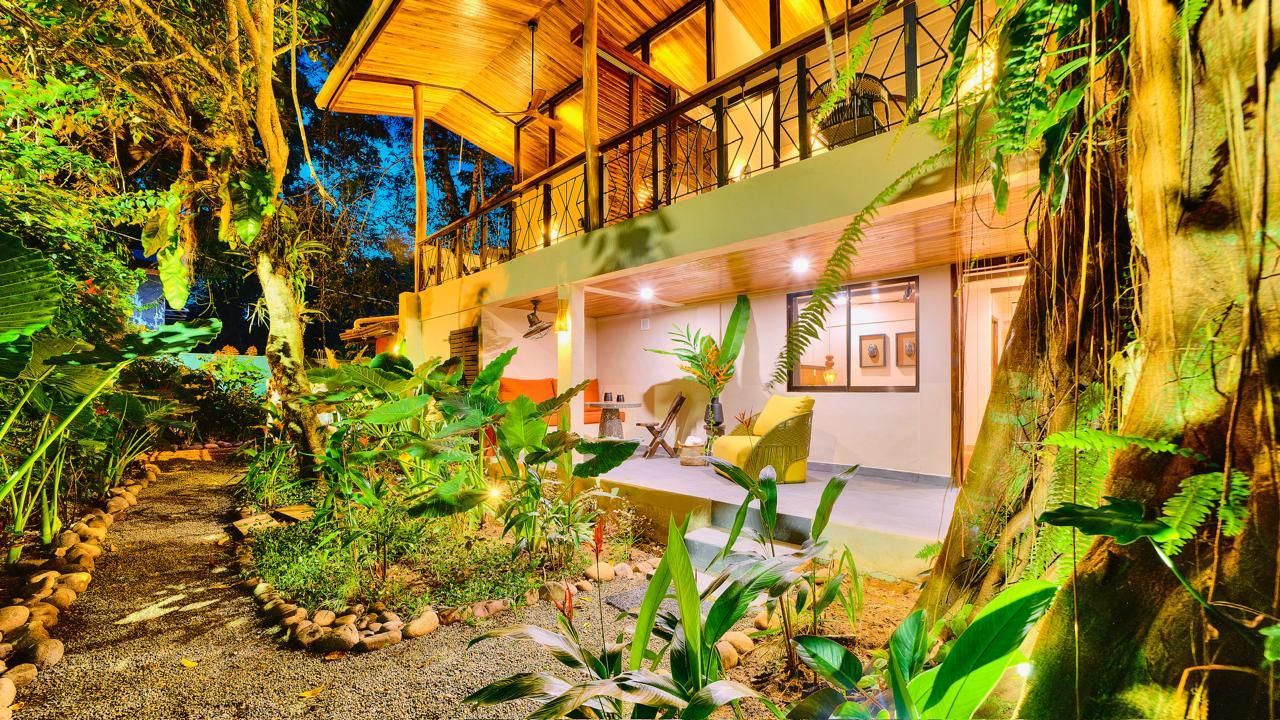 Tropical two-story building surrounded by lush greenery and a stone path, lit up at dusk.
