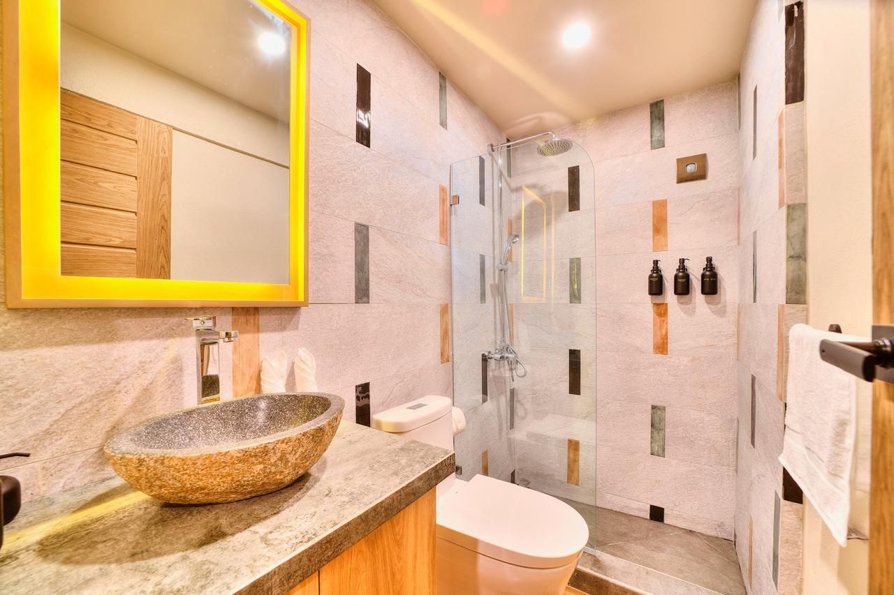Bathroom with stone sink, shower, and toilet, featuring neutral walls with vertical color accents.