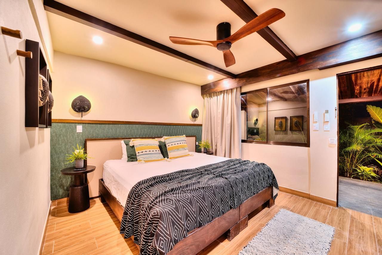 Bedroom with wooden beams, large bed, patterned blanket, window to outside, and ceiling fan.