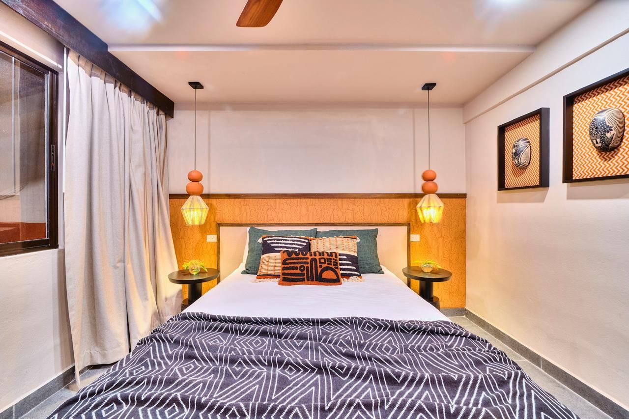 Bedroom with a bed, lamps, decorative masks on the wall, and curtains.