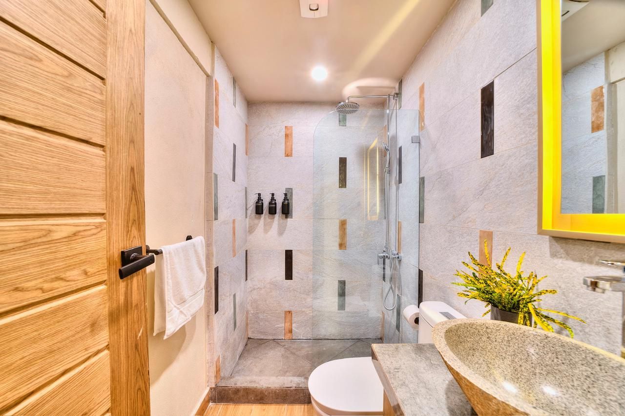 Bathroom with wood door, stone sink, glass shower, and patterned wall tiles.