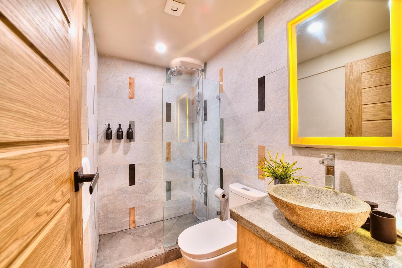 Bathroom with shower, toilet, and stone vessel sink. Wooden door and mirror frame.