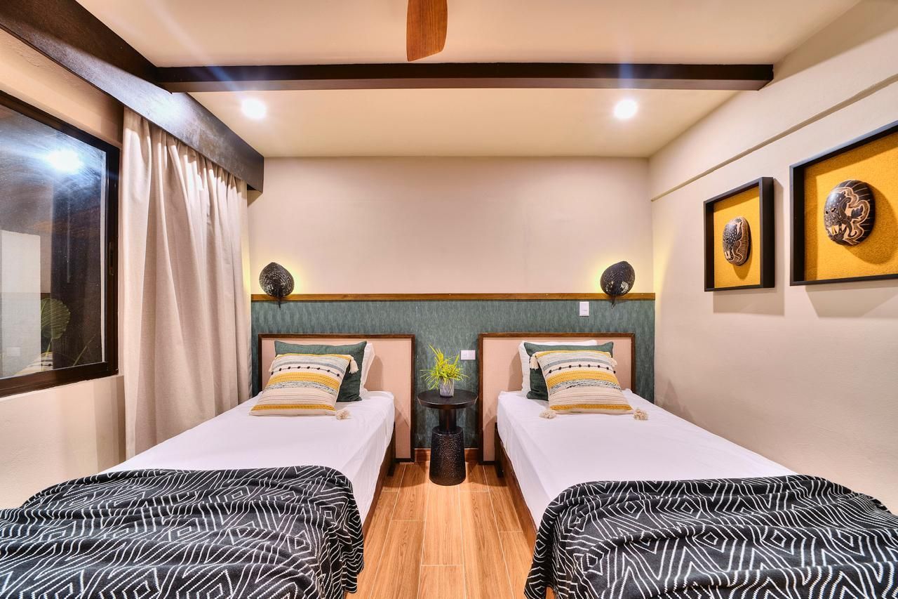 Two twin beds in a room with patterned blankets, decorative pillows, and artwork on the wall.
