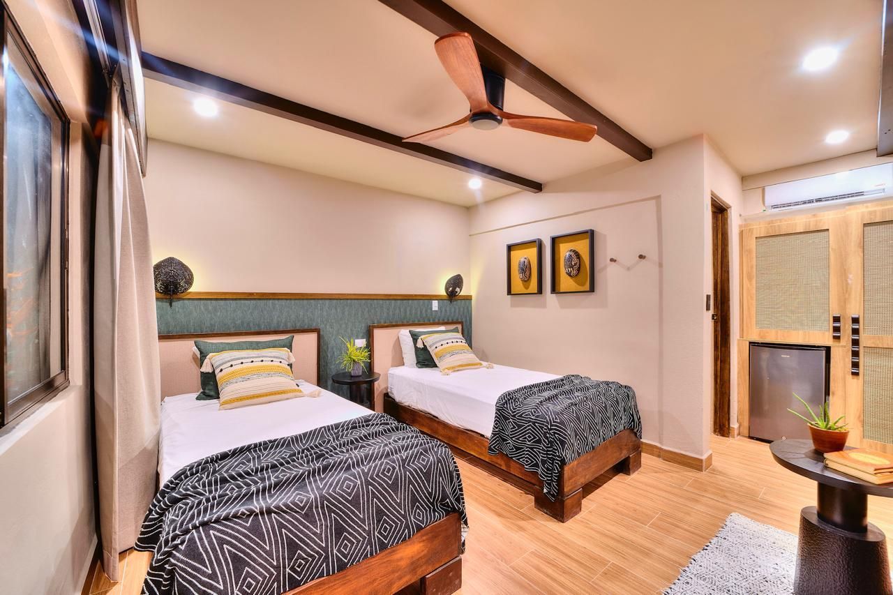 Two twin beds in a room with a ceiling fan, artwork, and small table.