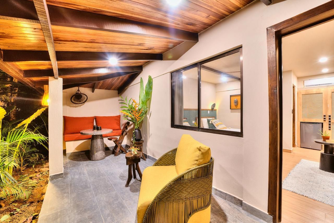 Patio with seating and window into bedroom. Red couch, yellow chair, wooden ceiling.