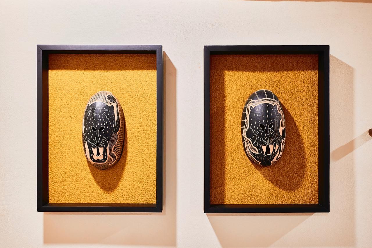 Two oval masks with white patterns, framed in black, mounted on golden textured backgrounds.