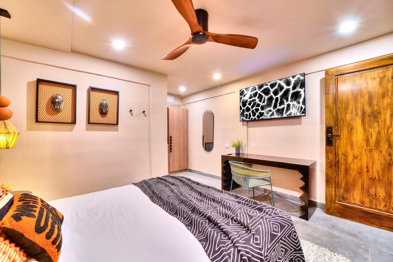 Bedroom with African-themed decor. Features bed, wooden furniture, artwork, ceiling fan, and a TV with giraffe pattern.