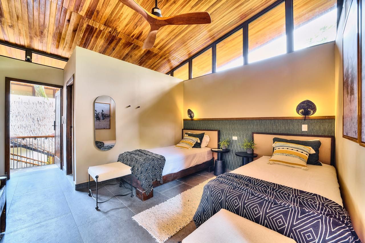 Bedroom with two twin beds, tan walls, wooden ceiling, and a view of an outdoor staircase.