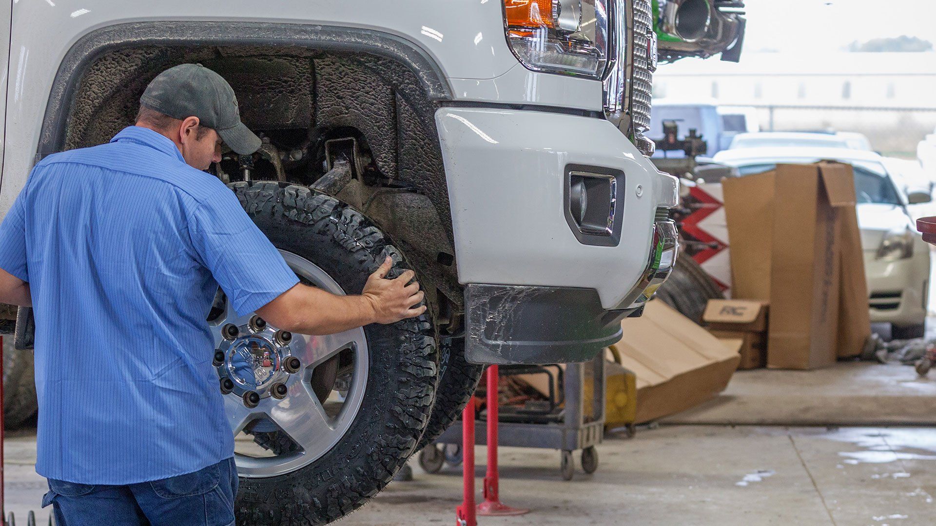A person in a blue shirt works on the wheel of a white truck inside a garage.