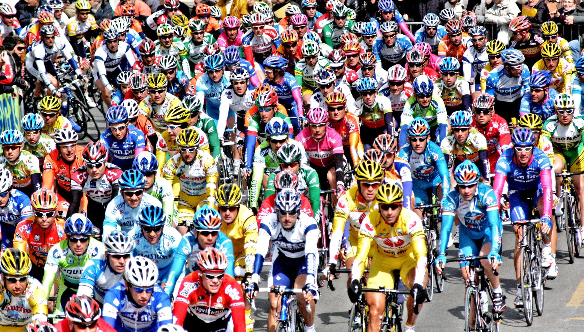 Cyclists in colorful jerseys racing in a crowded pack on a road during a bike race