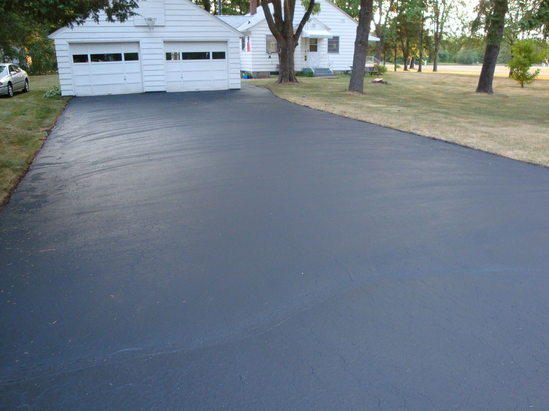 Newly paved black asphalt driveway leading to a white garage and house with green lawn.