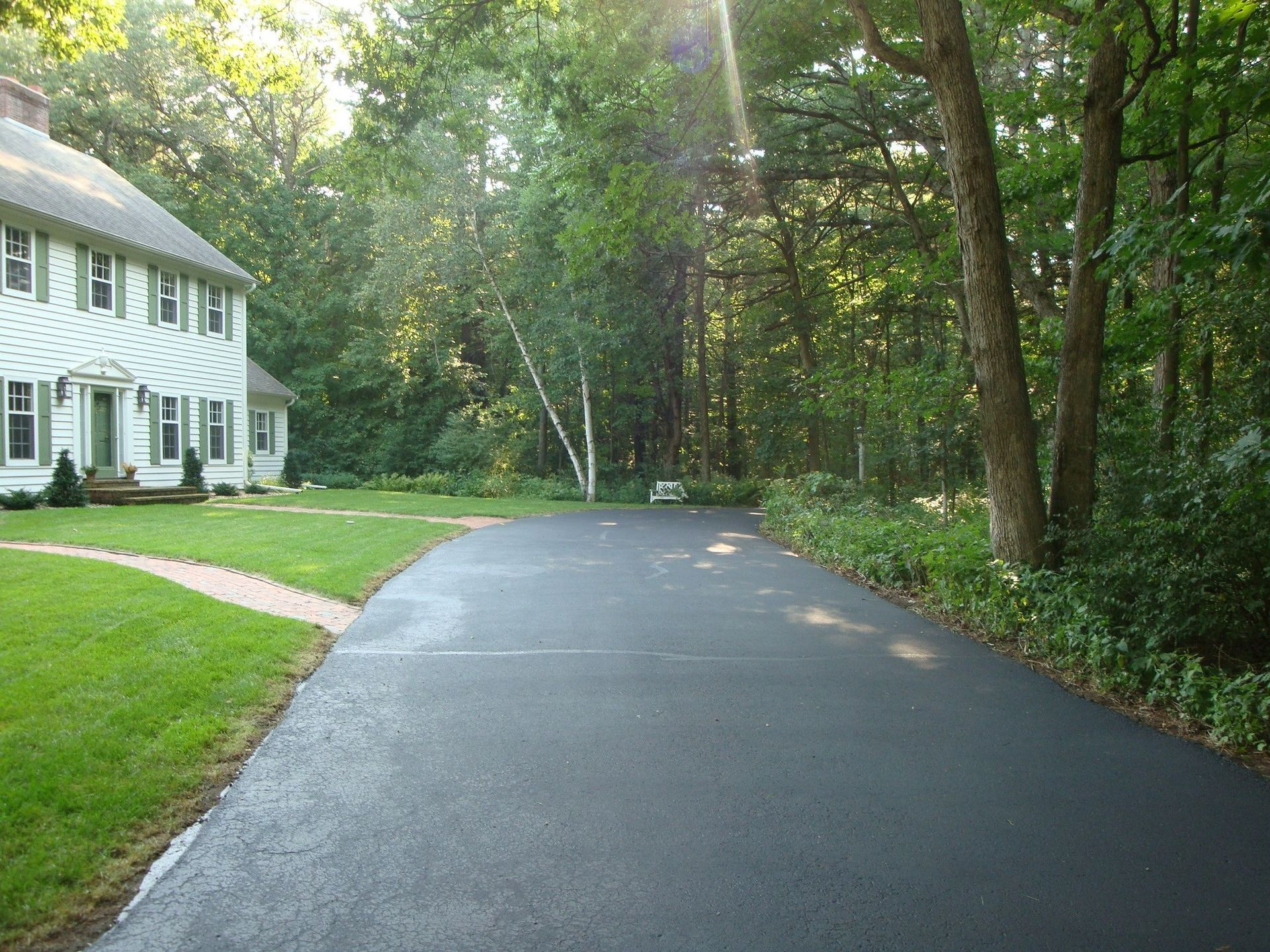 Driveway leading to a two-story house in a wooded setting.
