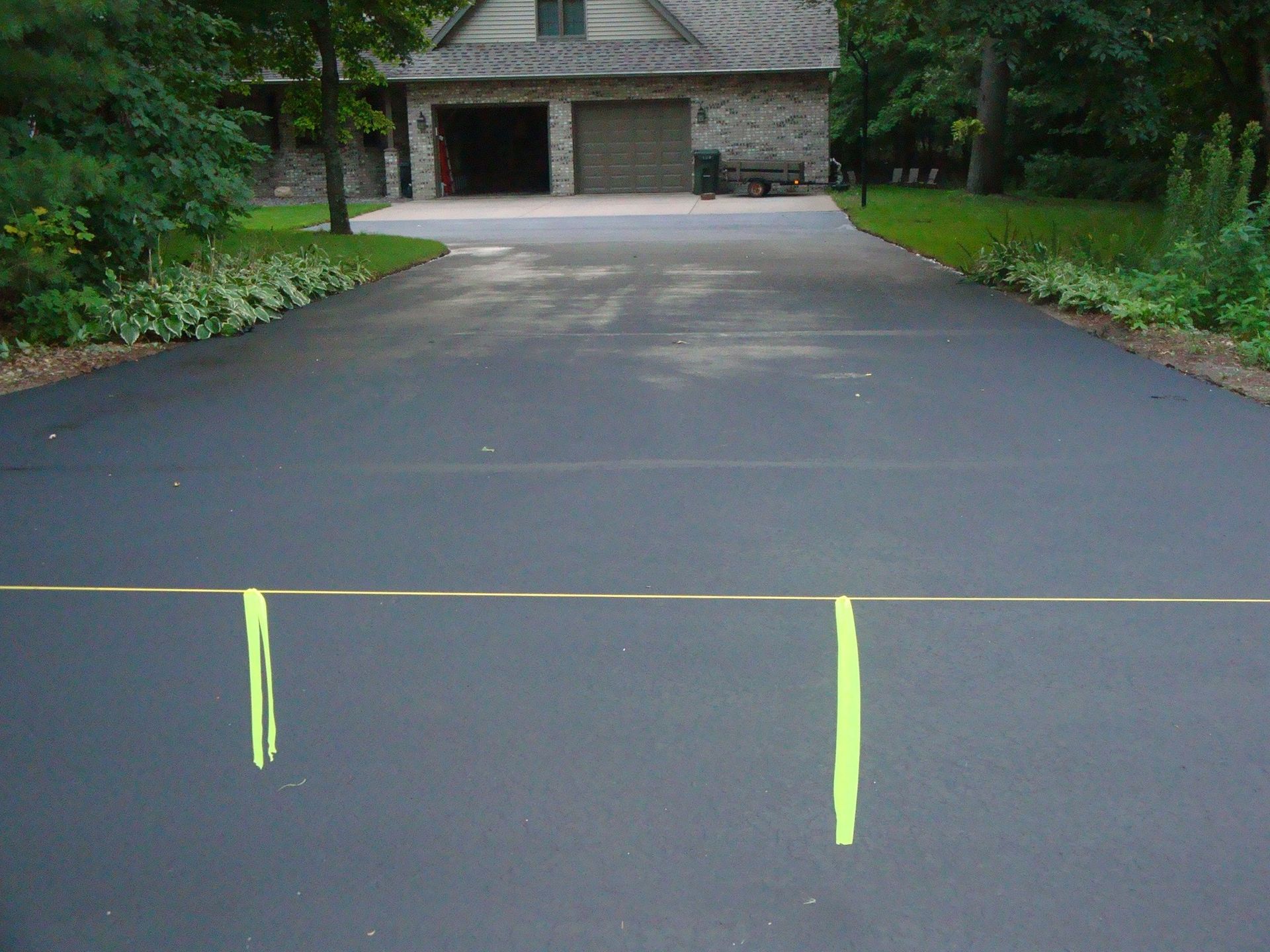 Asphalt driveway leads to a garage; yellow tape markers are on the driveway.