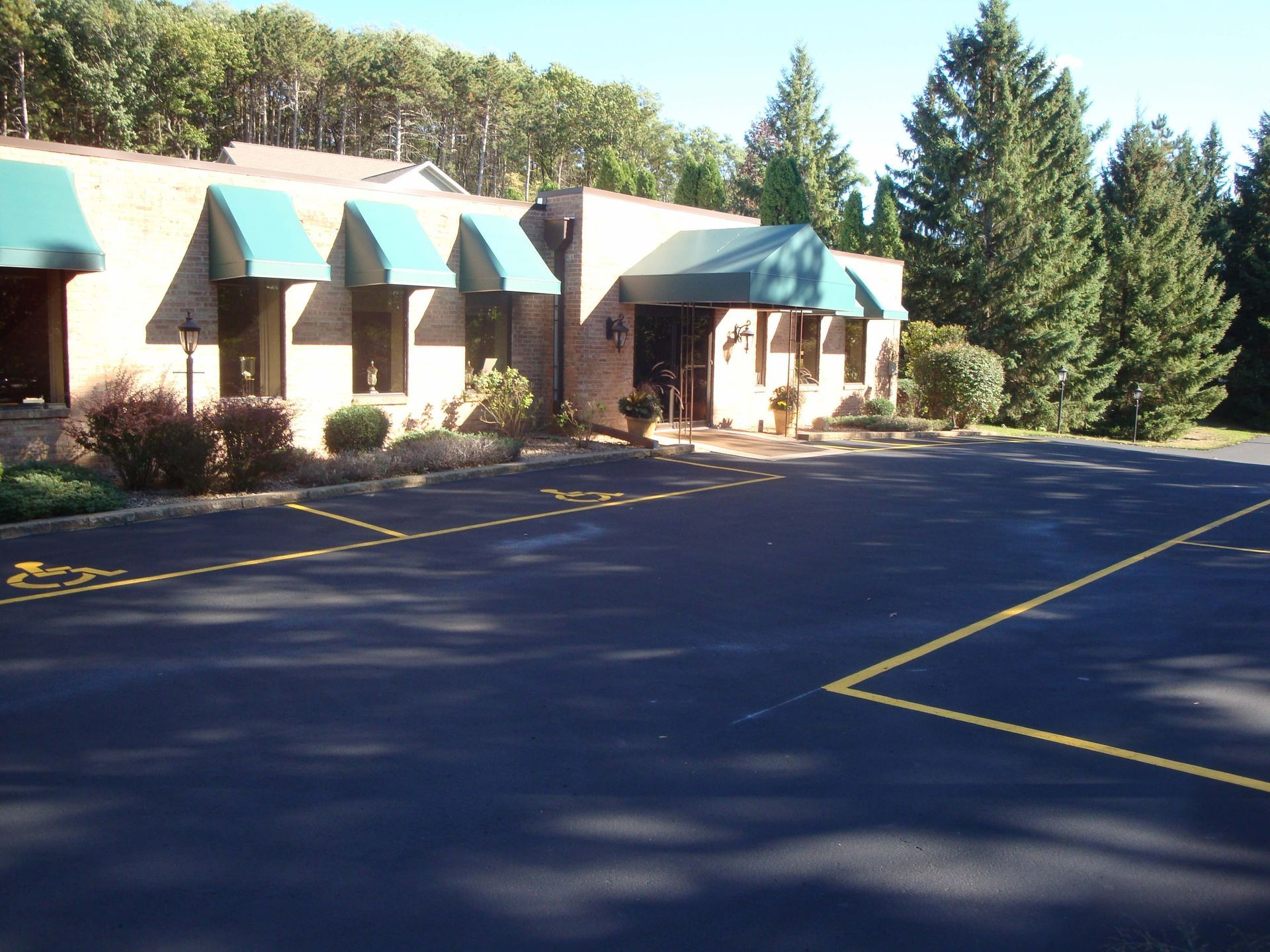 Exterior of a one-story brick building with teal awnings, bushes, and a paved parking lot.