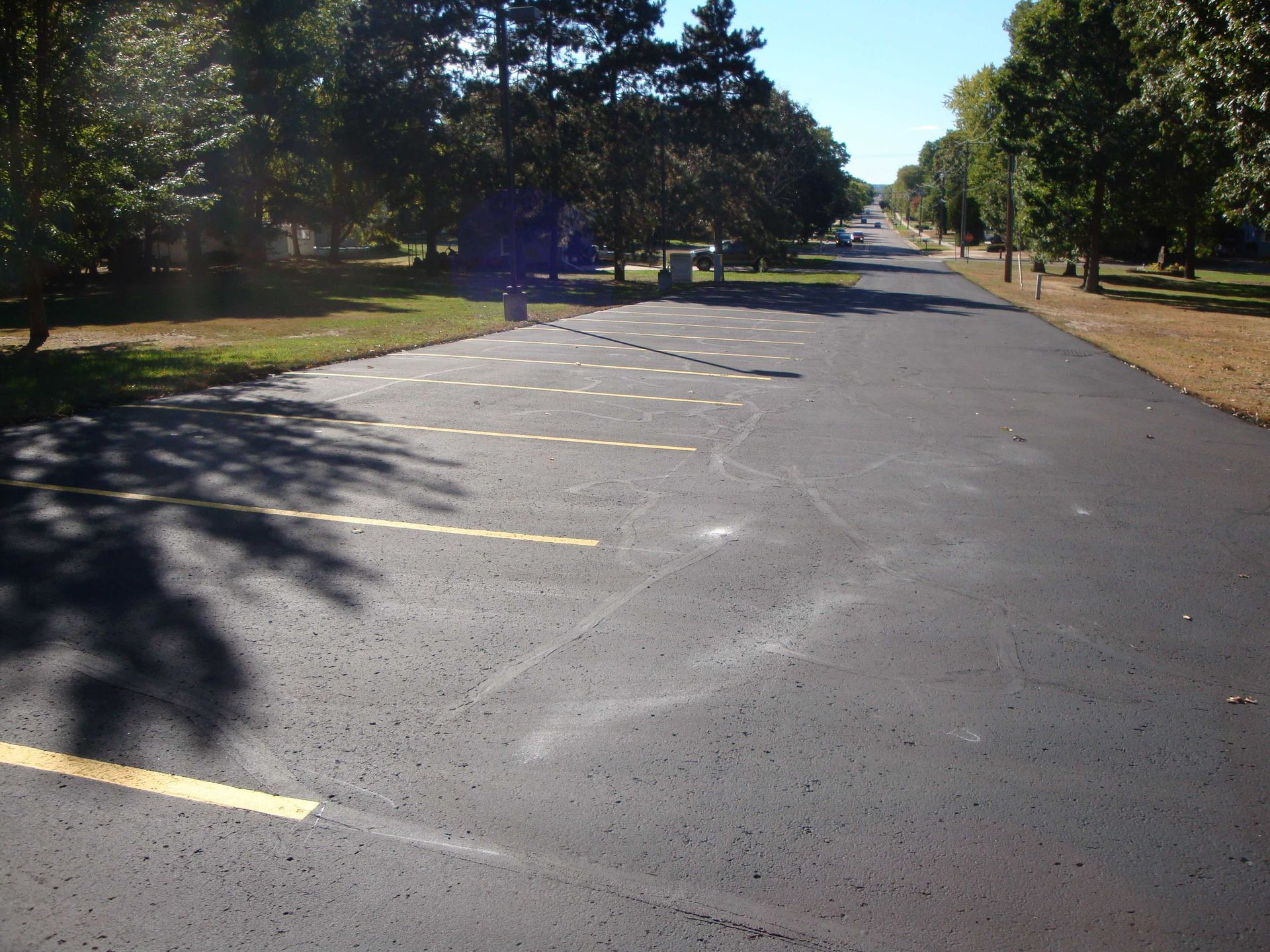 Parking lot with yellow lines, green grass, trees, and a road extending into the distance.