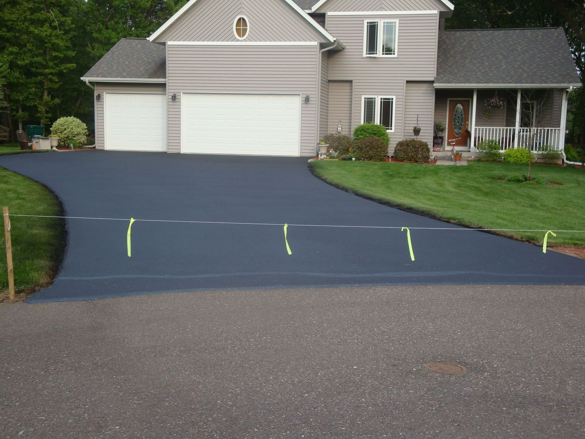 Newly paved dark asphalt driveway leading to a two-story house with white garage doors.