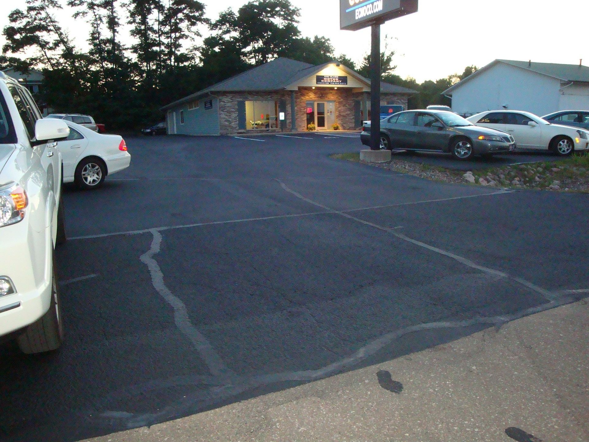Car parked in front of a business with a sign, trees, and other cars in a paved area.