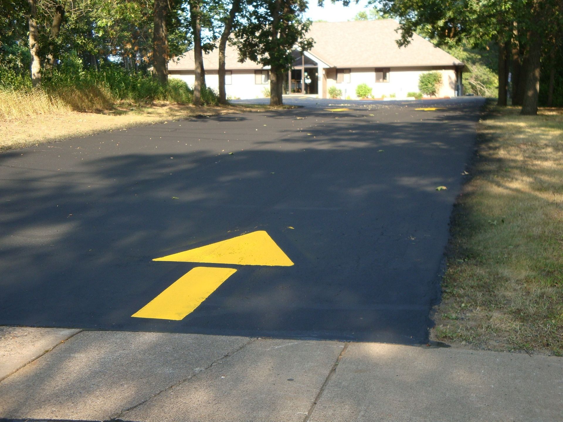 Yellow arrow painted on asphalt driveway, pointing towards a low building.