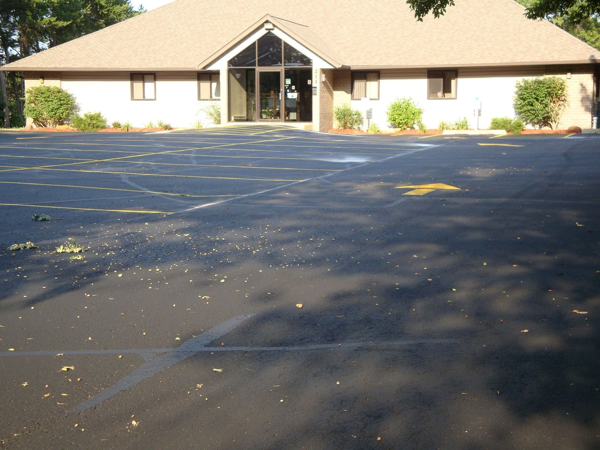 Building with a dark asphalt parking lot; sunlight casts shadows.