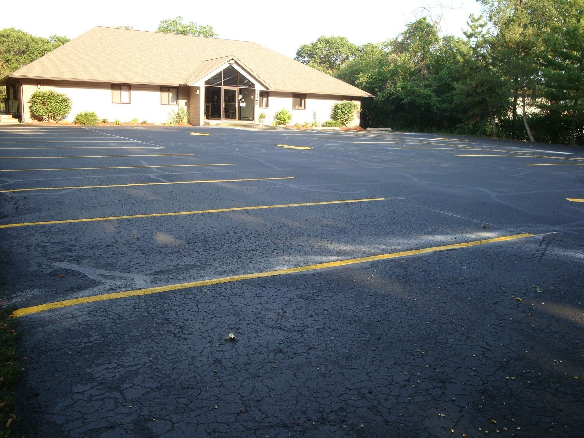 Paved parking lot in front of a one-story building with a brown roof and glass doors.