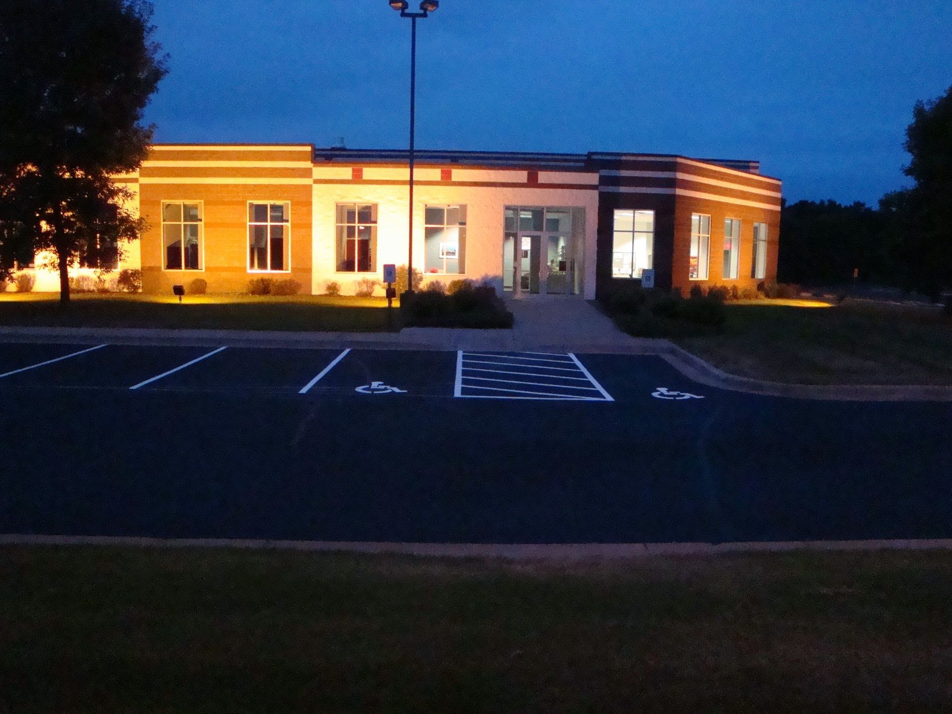 Exterior of brightly lit modern building at dusk with accessible parking spaces.