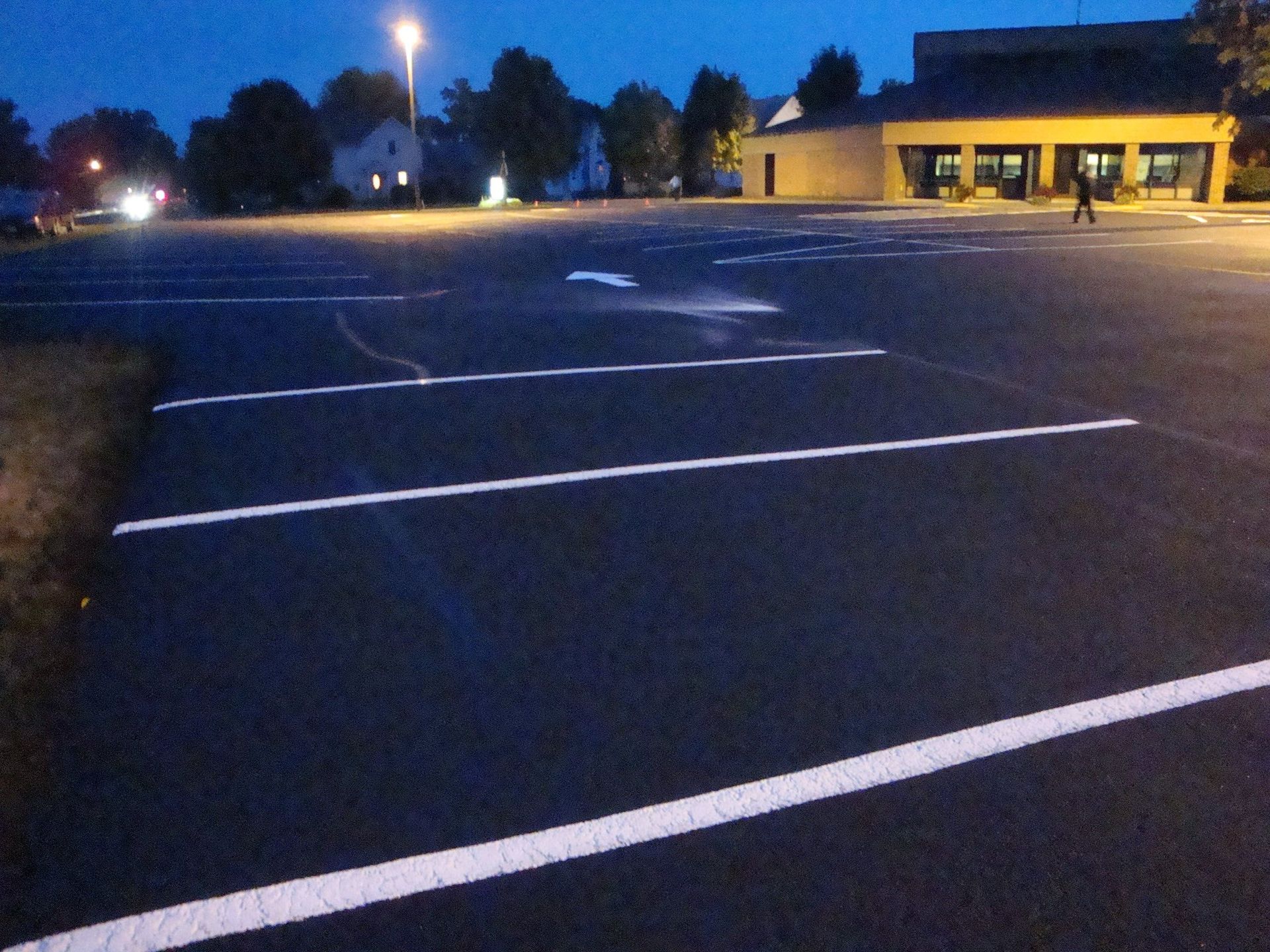 Dark asphalt parking lot with white lines, streetlights, and a building at dusk.