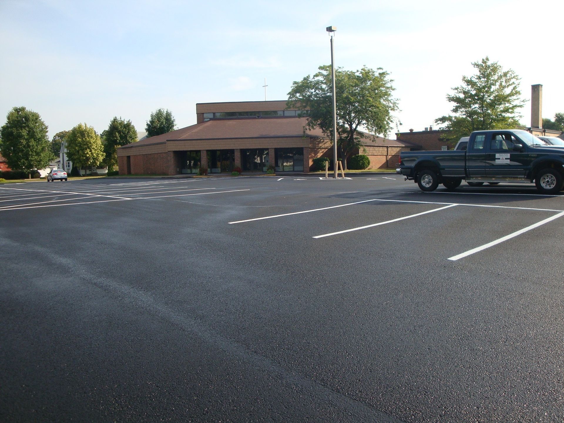 Newly paved parking lot with white parking lines in front of a brick building and a truck.