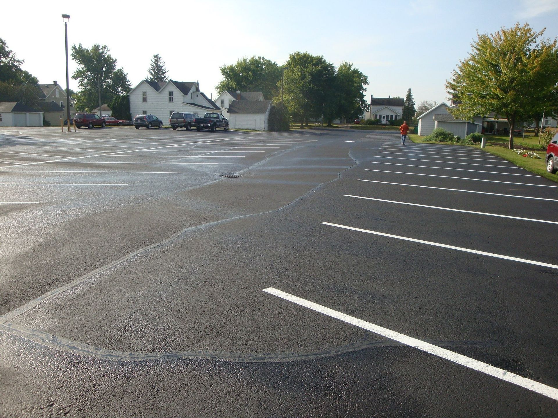 Newly paved parking lot with white lines, buildings, and a person walking.
