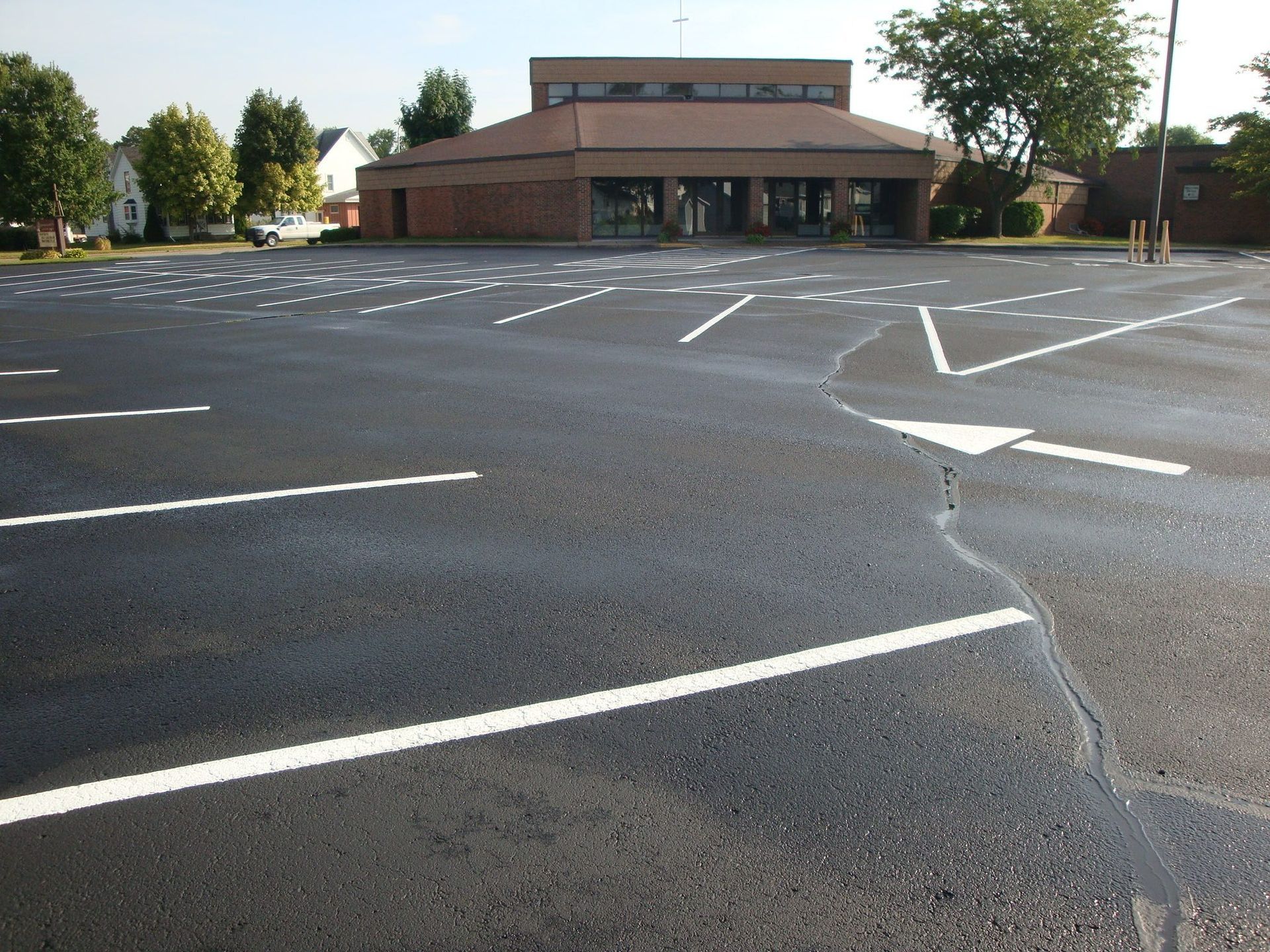Empty black asphalt parking lot with white painted lines and a brick building in the background.