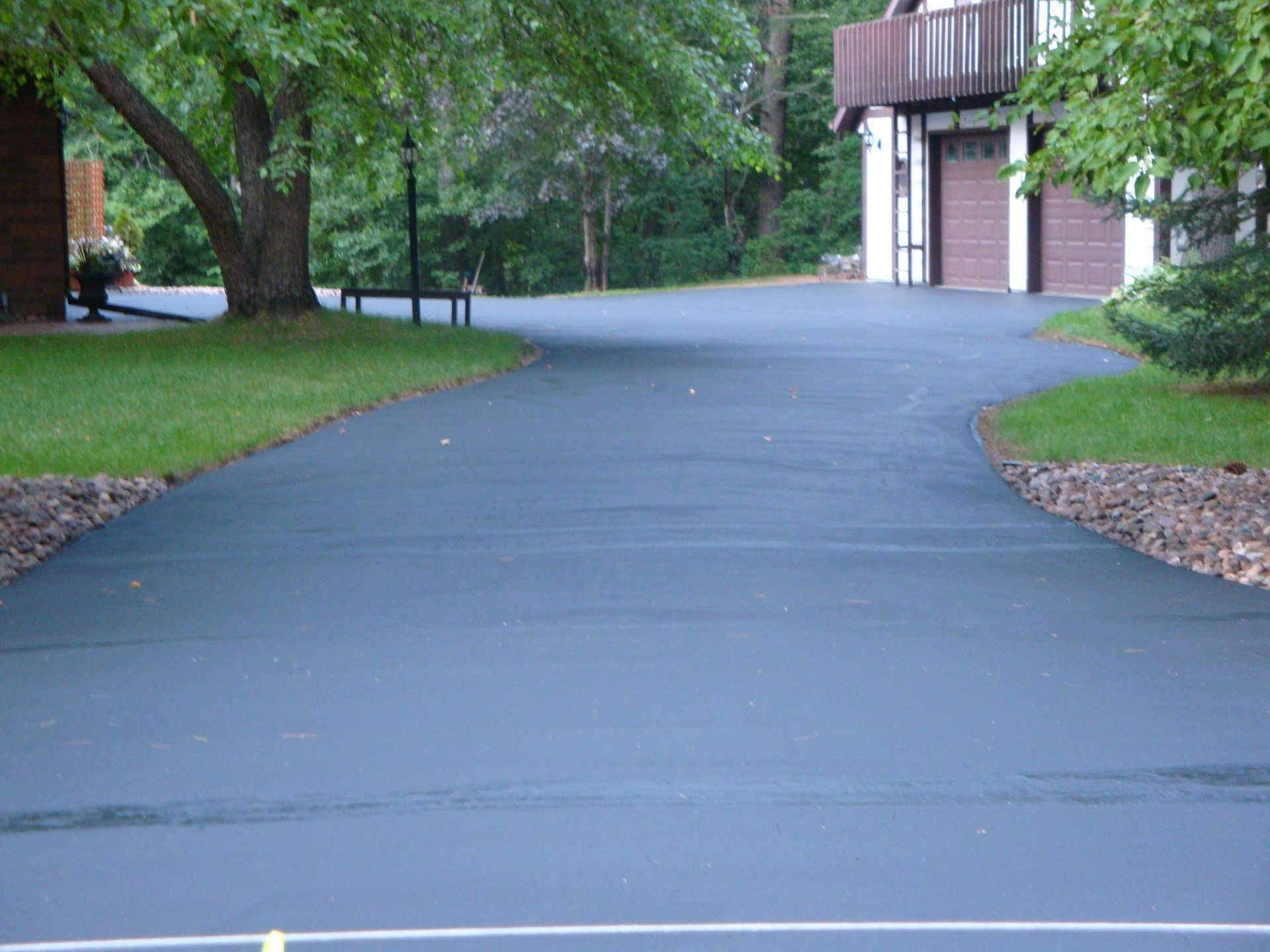 Paved driveway curving towards a house with brown garage doors, bordered by grass and landscaping.