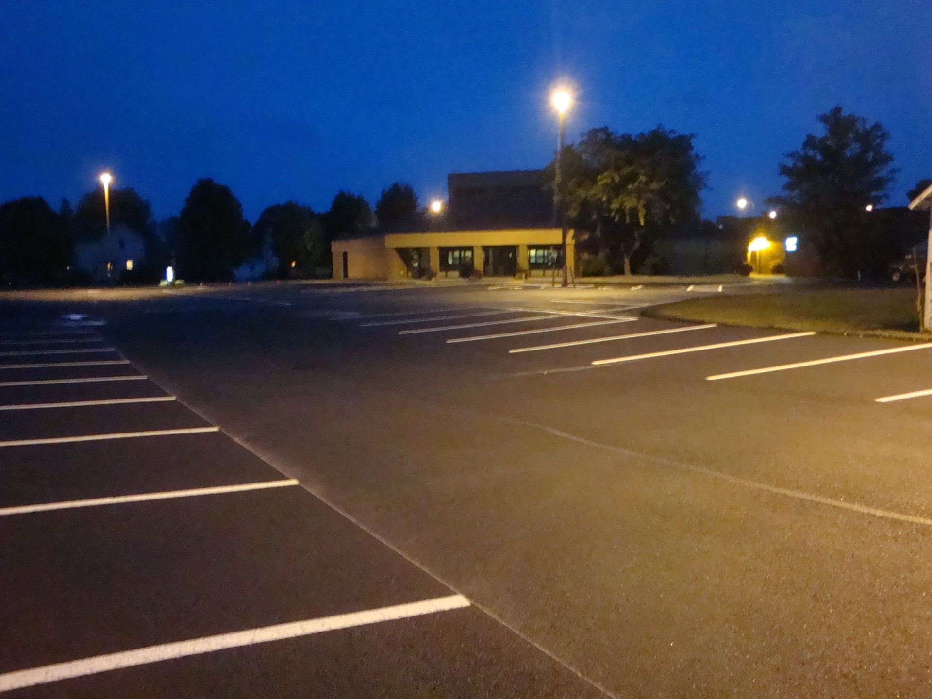 Empty parking lot at dusk with white painted parking space lines and a building in the background.