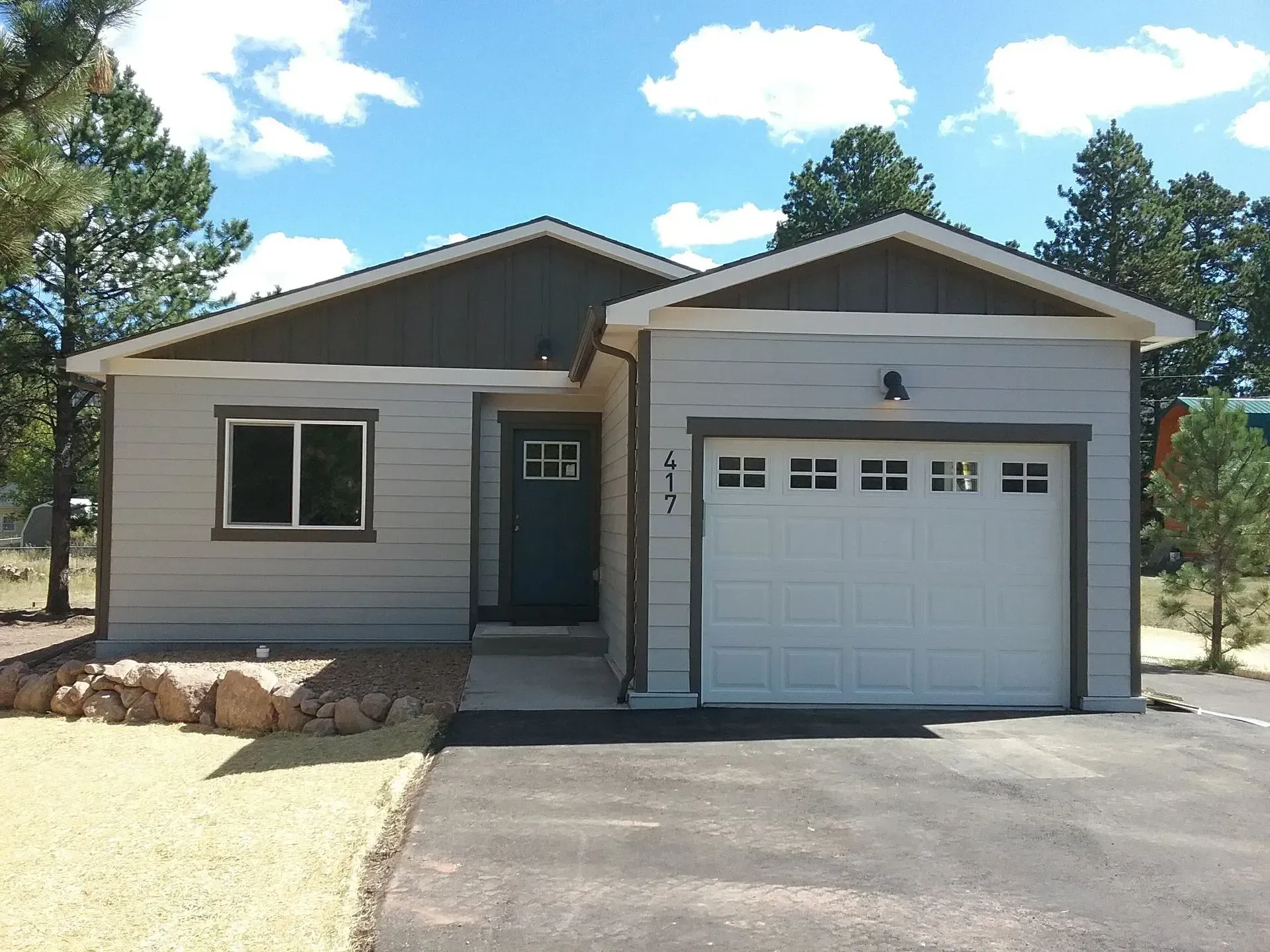 Gray and brown single-story house with a white garage door, small front yard, and blue door.