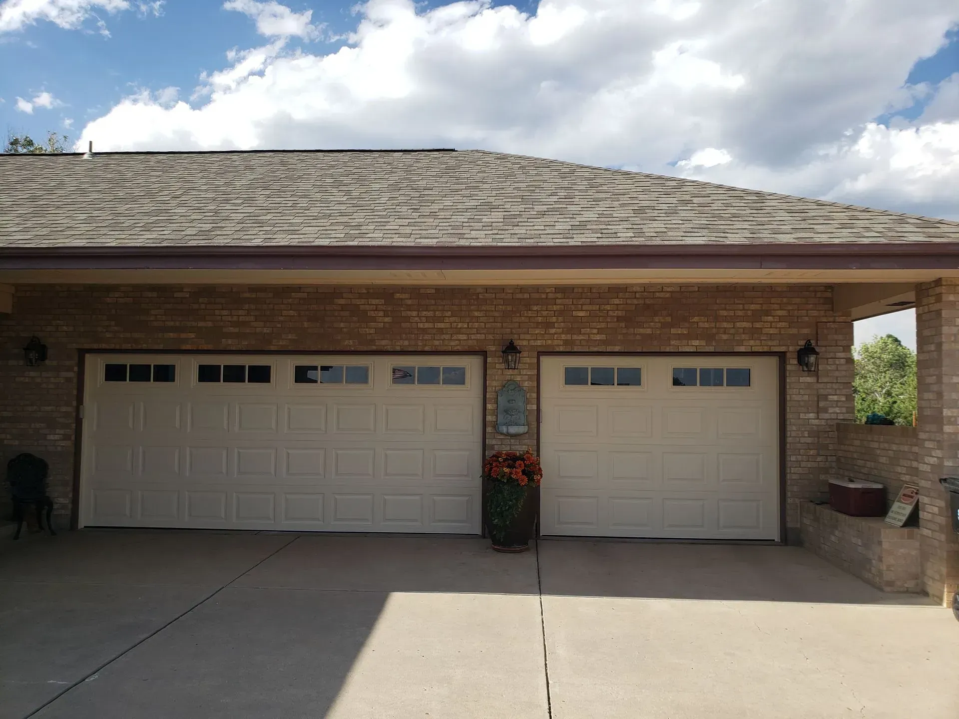 Two beige garage doors in a brick building under a cloudy sky.