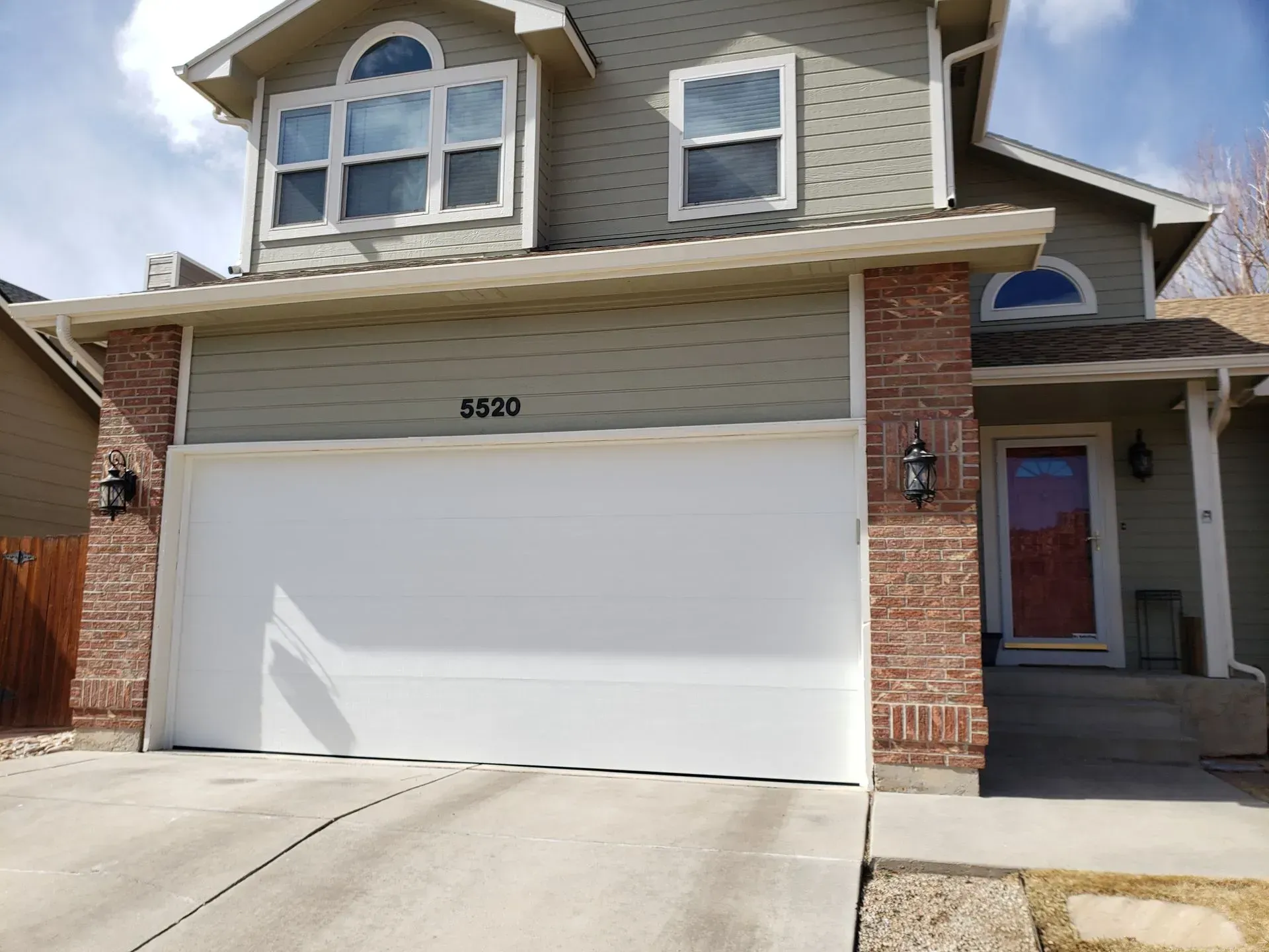 Two-story house with a white garage door, red brick accents, and green siding.
