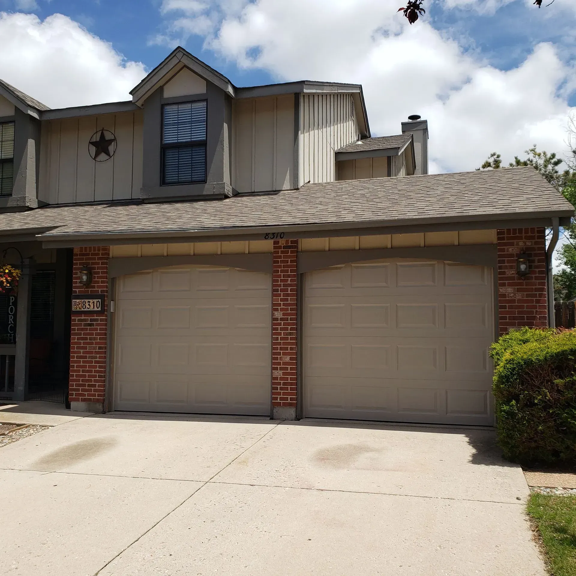 Two-story house with beige garage doors and brick accents, concrete driveway.