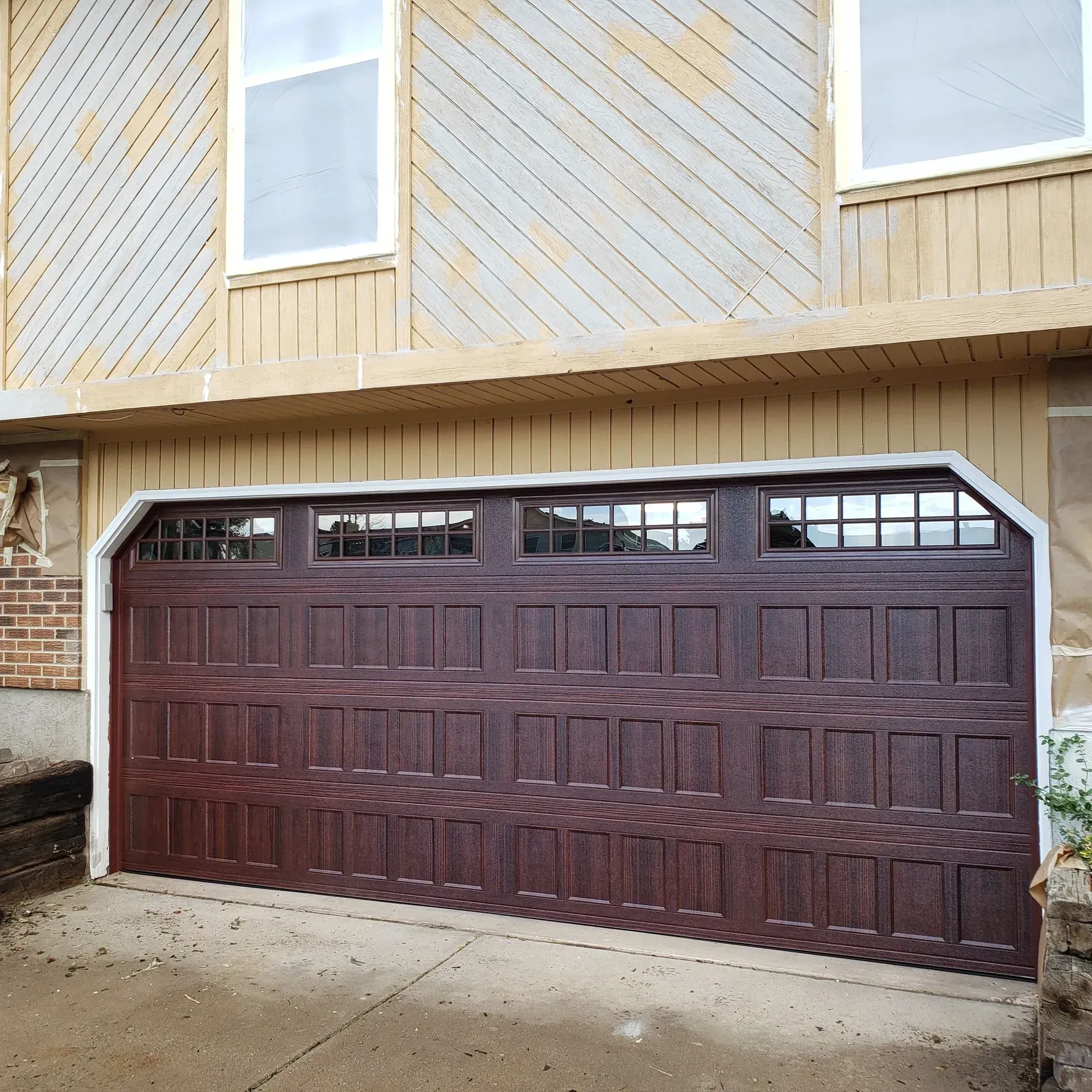 Brown garage door with windows, on a house with wood siding.