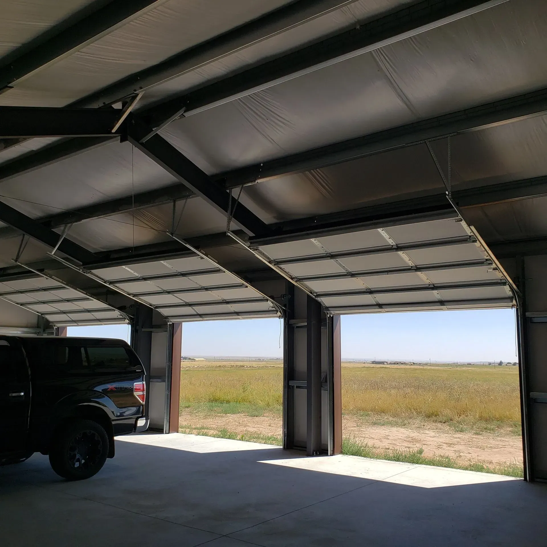 Steel-framed building with open garage doors; a black truck is parked inside.