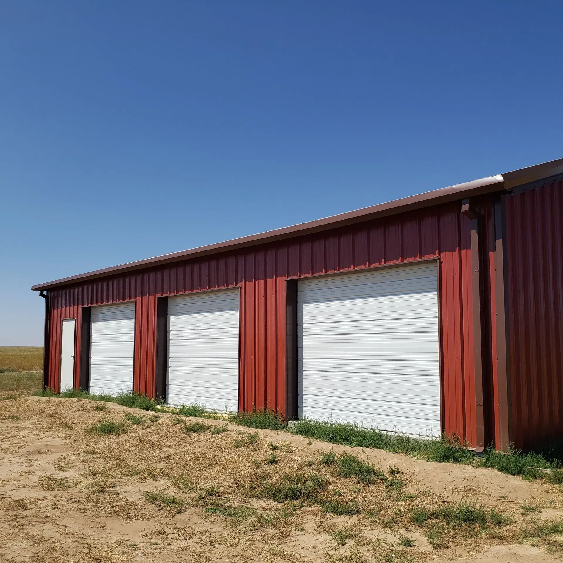 Red metal building with white garage doors against a blue sky.