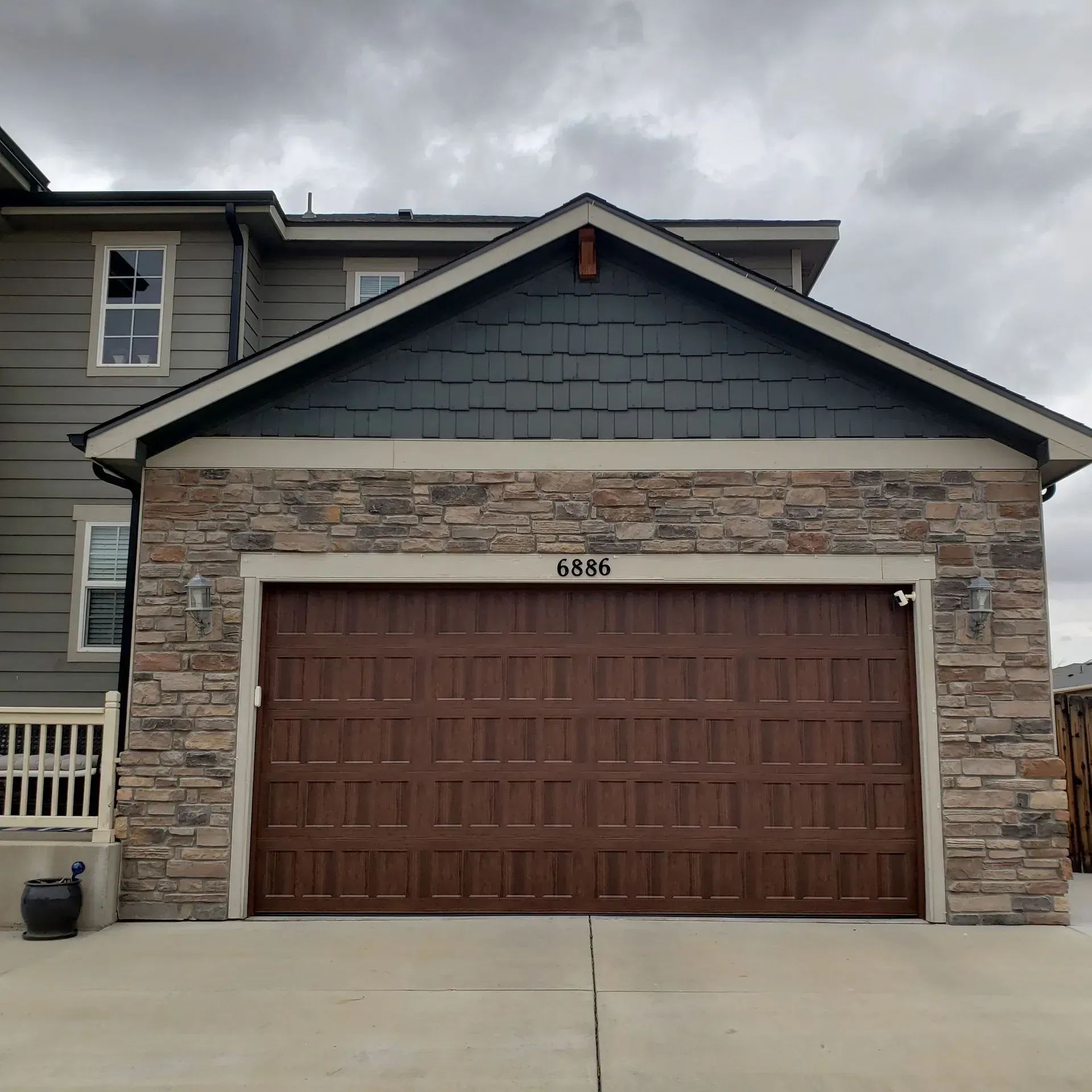Brown garage door with stone and dark green trim on a house under a cloudy sky.