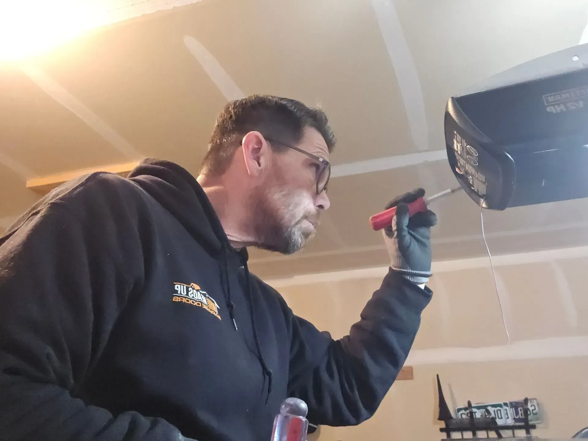Man in black hoodie repairs garage door opener with a screwdriver.