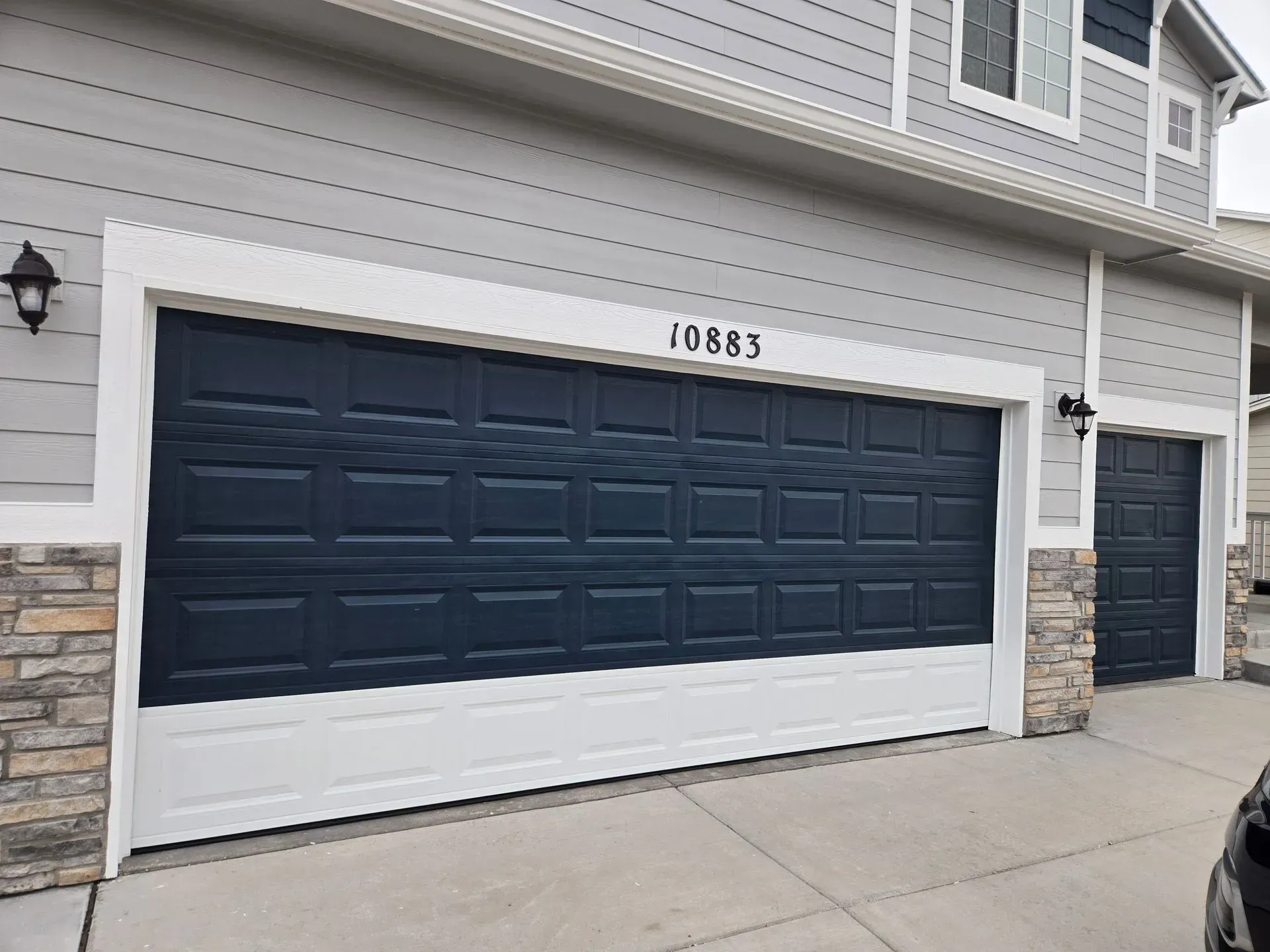 Navy blue garage door with white trim, address 20883, and two sconce lights on a house.