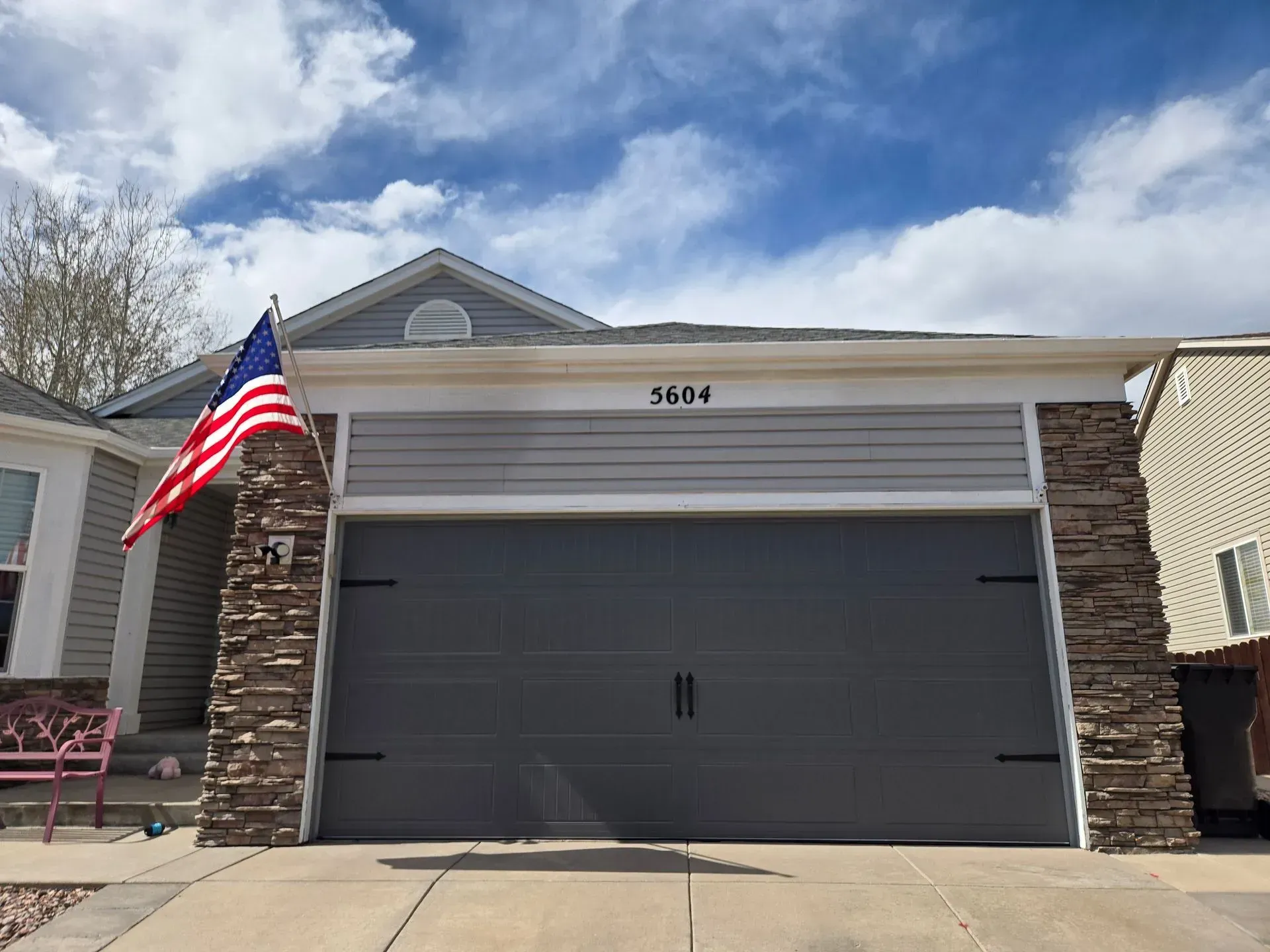 House with gray garage door, American flag, blue sky, and stone accents. Number 5634 above the garage.