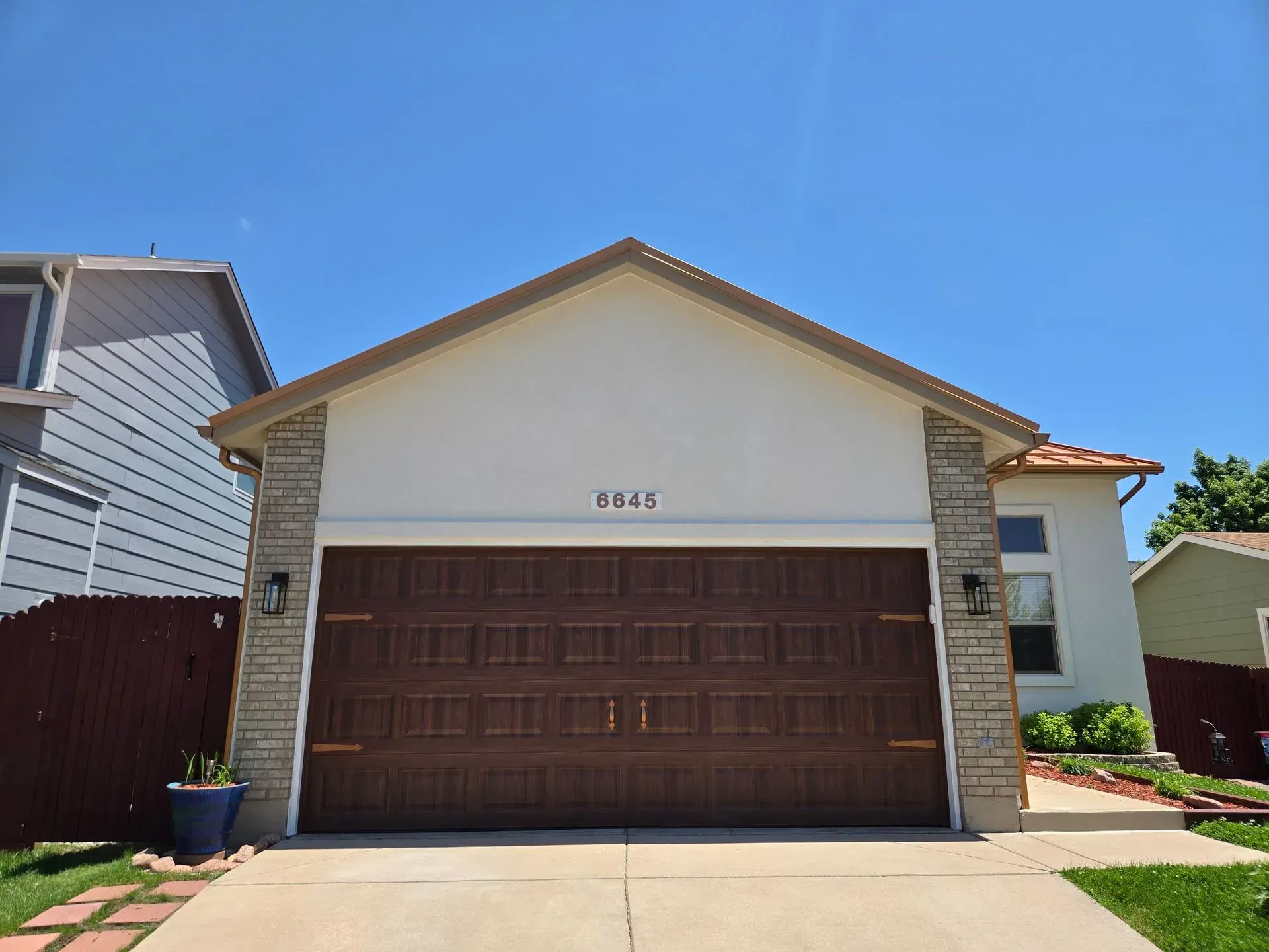 Brown garage door on a light-colored house under a clear, blue sky. House number 